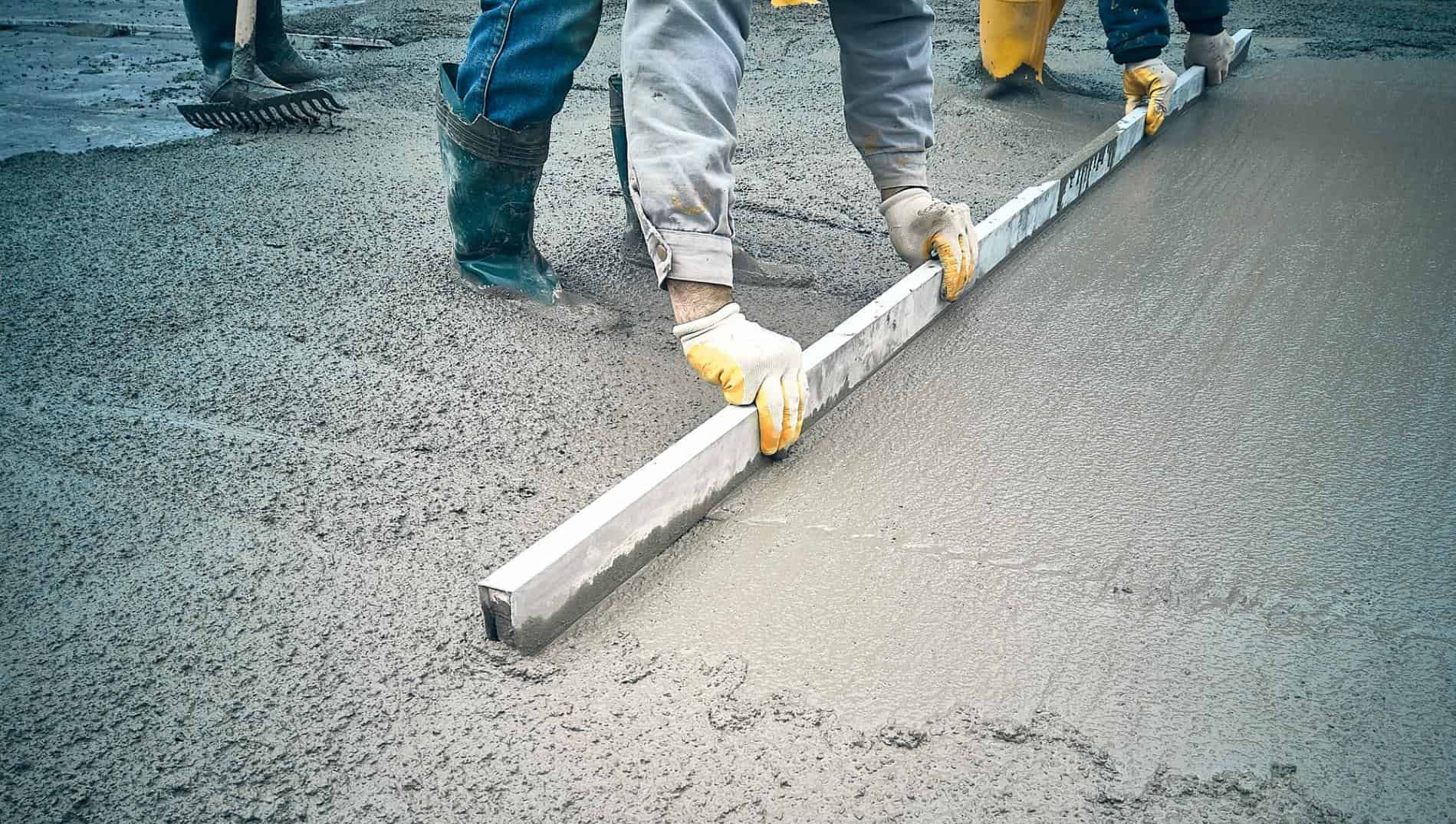 Arbeidere avretter fersk betong med rettholt for å sikre jevn og slitesterk overflate.